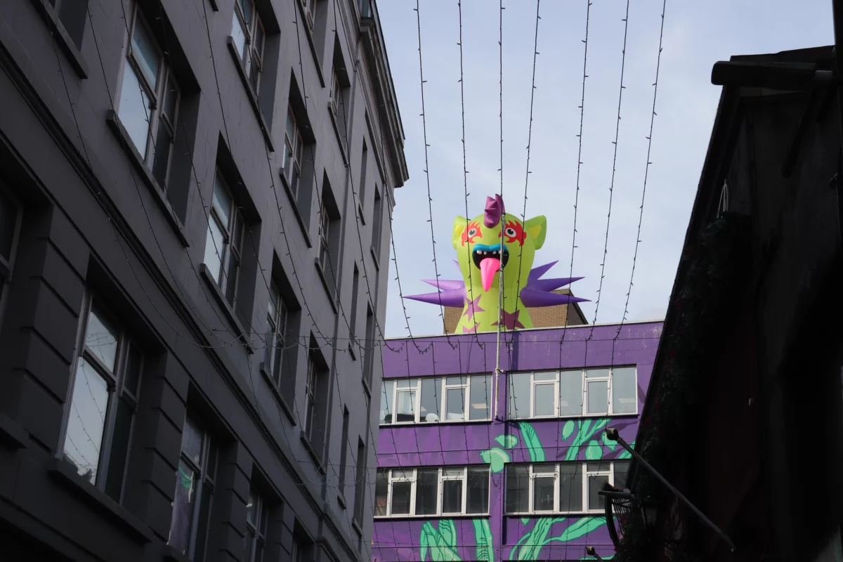 Kleurrijk opblaasmonster op een dak boven een smalle straat in Belfast