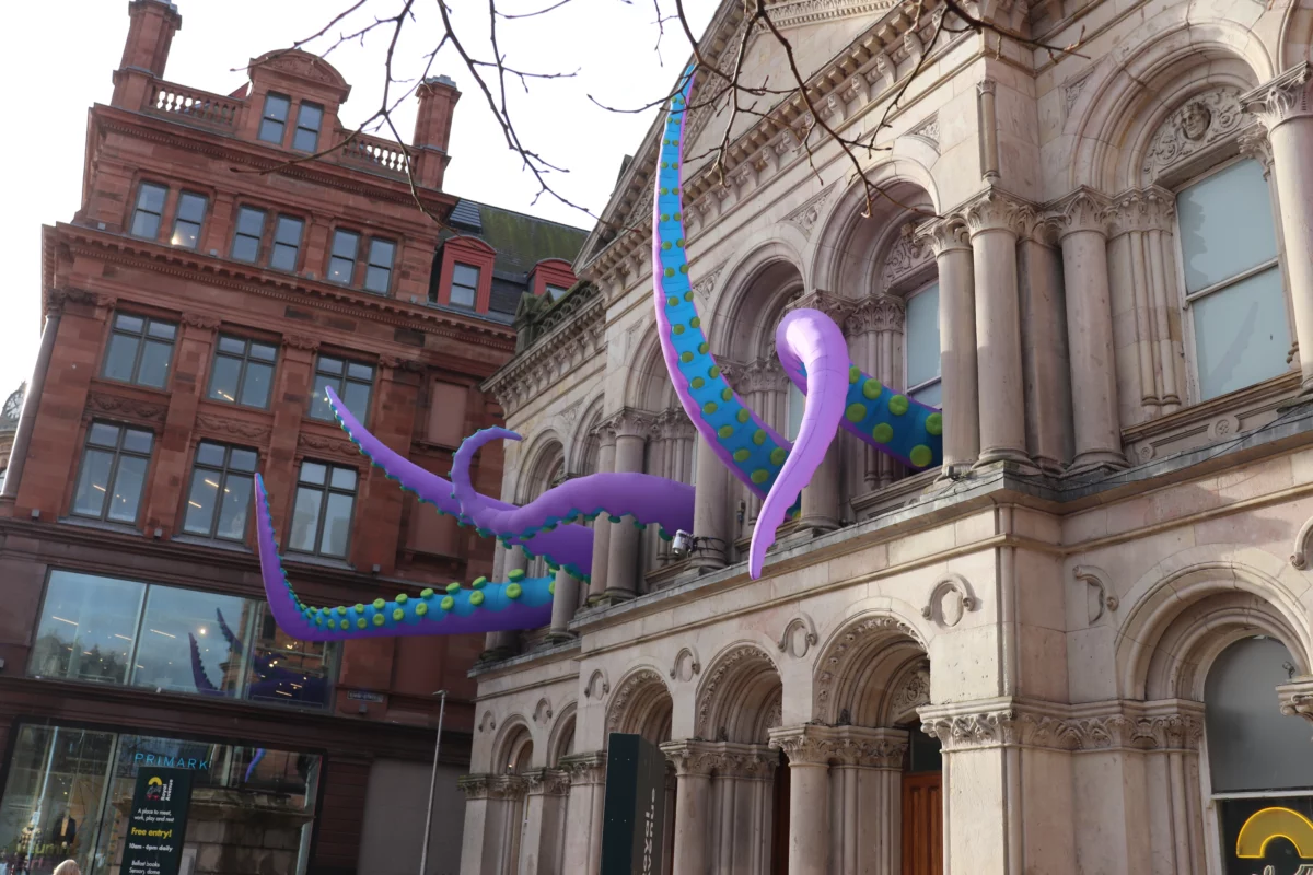 Paarse tentakels met groene stippen steken uit een historische gevel in Belfast
