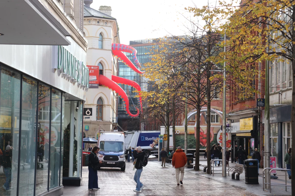 Rode monstertentakels boven een winkelstraat met herfstbomen in Belfast